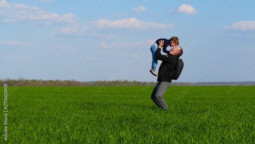 A happy child runs across the green grass into the arms of his father, who raises the child in his arms and throws him up A happy child runs across the green grass into the arms of his father, who raises the child in his arms and throws him up