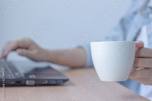 Woman drinking hot coffee and using laptop on office desk.