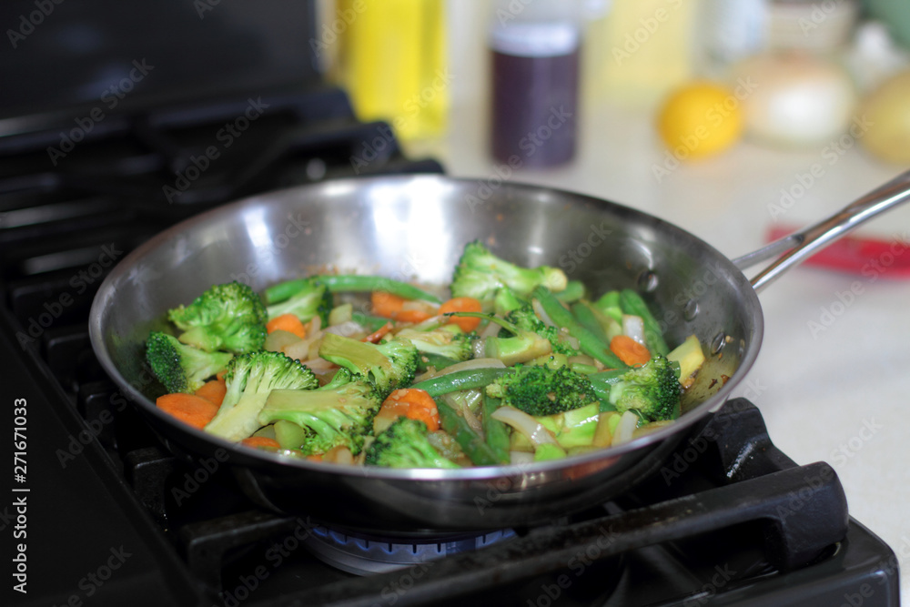 Stir fry vegetables cooking in a stainless steel pan on a natural gas stove. Stir fry vegetables cooking in a stainless steel pan on a natural gas stove.
