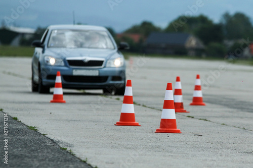 The detail of the traffic cones on the concrete area. They are used for testing of the cars. The blurred car is behind the cones. 