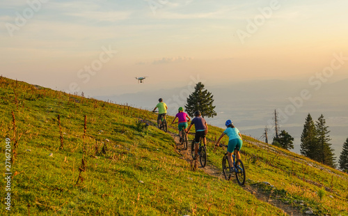 Small drone flies along a group of tourists mountain biking on a sunny evening.