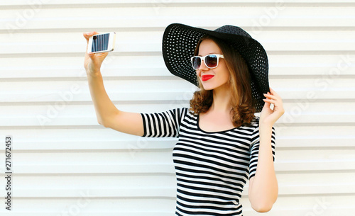 Close-up woman taking selfie picture by phone on white wall background