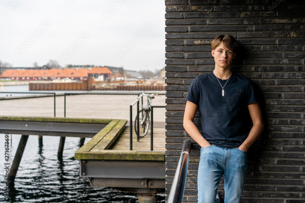 Denmark, Copenhagen, portrait of young man leaning standing at a wall at the waterfront Denmark, Copenhagen, portrait of young man leaning standing at a wall at the waterfront