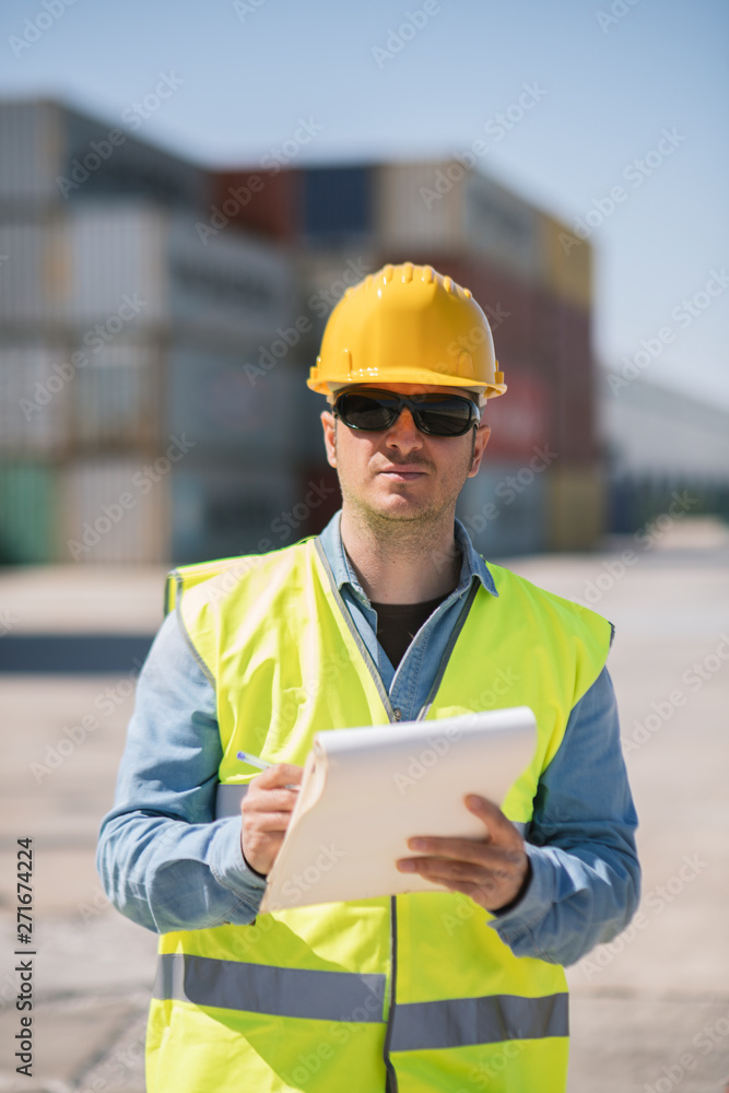 Portrait of a worker with a notepad near cargo containers on industrial site Portrait of a worker with a notepad near cargo containers on industrial site