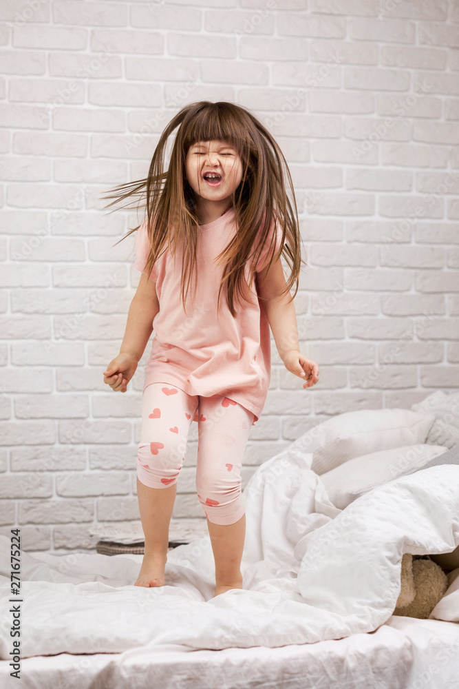 Naklejka premium cute little child girl fooling around in bed. child jumping on bed