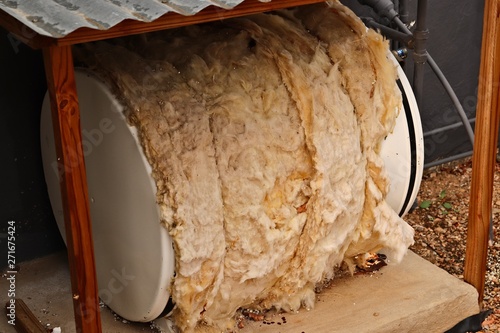A small residential water boiler (geyser) with old insulation material covering it.  House maintenance and plumbing concept image. 
