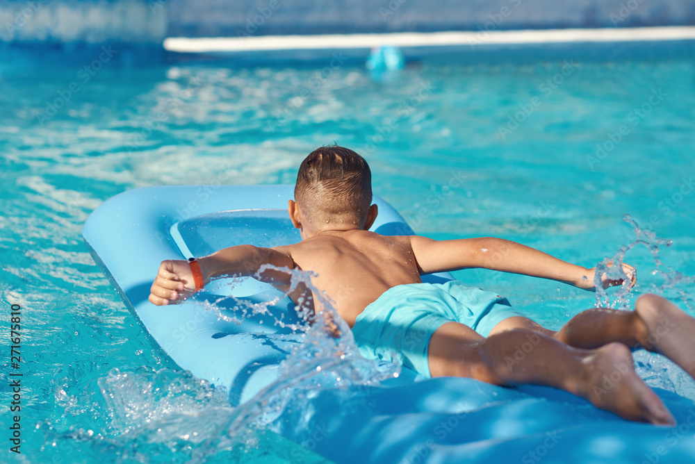  Caucasian boy  is  laying on blue  inflatable mattress at hotel swimming pool. He is enjoying his summer vacations.