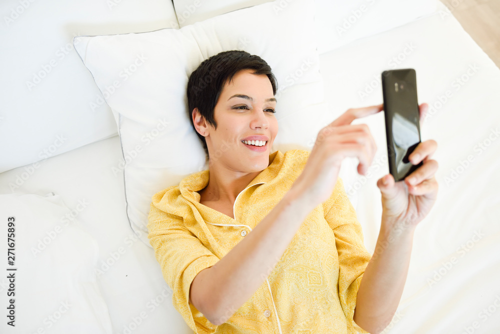 Smiling young woman using cell phone in bed