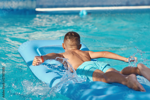  Caucasian boy  is  laying on blue  inflatable mattress at hotel swimming pool. He is enjoying his summer vacations. © Artem
