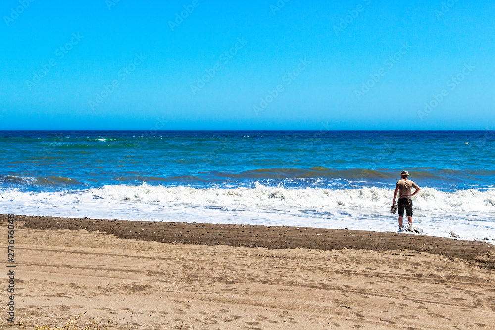 Rear view of an unidentified male tourist on a sandy beach at Torre de Benagalbon, Province of Malaga, Andalusia, Spain Rear view of an unidentified male tourist on a sandy beach at Torre de Benagalbon, Province of Malaga, Andalusia, Spain