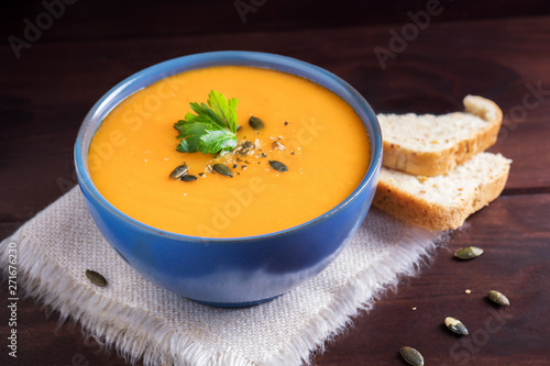 Pumpkin soup in a bowl served with parsley, olive oil and pumpkin seeds. Vegan soup. Dark wooden background.