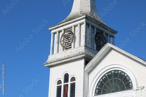 Old weathered wooden white New England church with steeple and clock