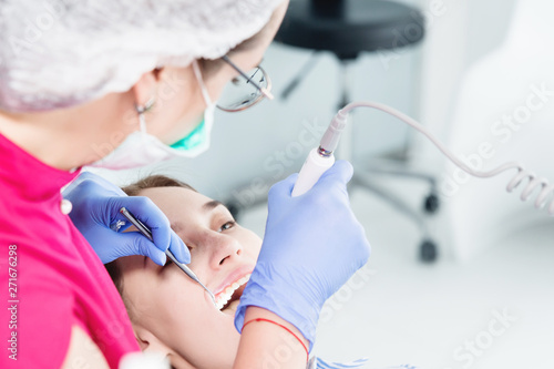 Close-up A professional dentist woman in glasses and overalls examines the oral cavity of a young girl in the dental chair using an intraoral stamotological video camera with LED illumination