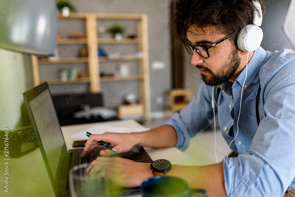 Young modern bearded man working with laptop computer indoors