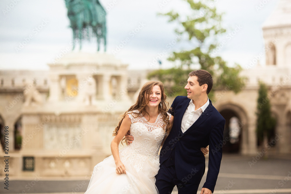 Young beautiful stylish pair of newlyweds walking by the Fisherman's Bastion in Budapest, Hungary Young beautiful stylish pair of newlyweds walking by the Fisherman's Bastion in Budapest, Hungary