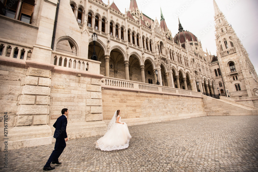 Bride and groom hugging in the old town street. Wedding couple walks in Budapest near Parliament House.