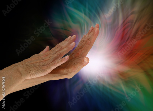 Sending light and healing energy out where it is needed - female hands appearing to push out white light from the palm with darkness on left and multiple colours around the light source