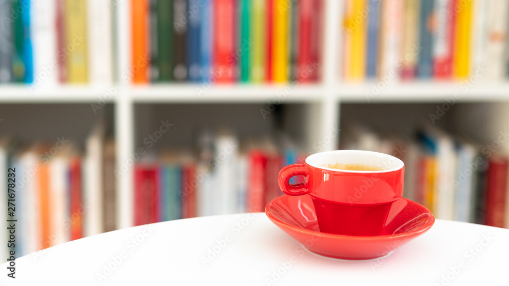 A small red cup on a background of books in a home room. Coffe time A small red cup on a background of books in a home room. Coffe time