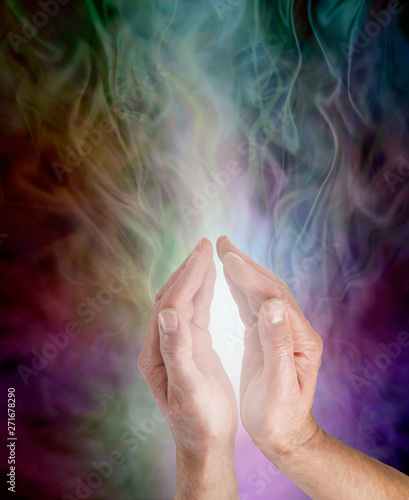 Bringing light into the darkness - male hands cupped around gentle white light rising up against an ethereal gaseous multicoloured background with copy space 