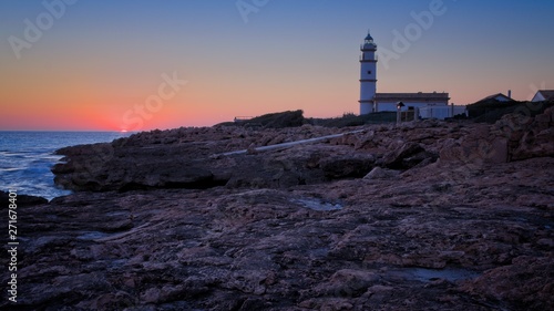 Lighthouse Far del cap ses salines at sunset, rocks, building, setting sun, beautiful golden sky, Mallorca, Spain.