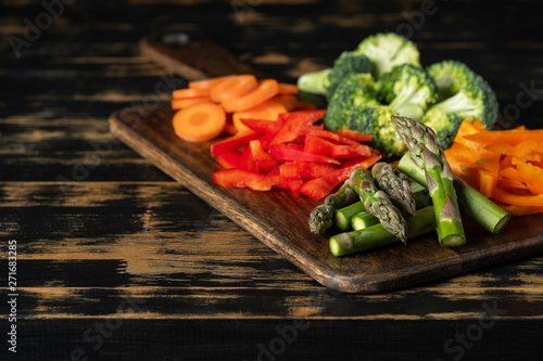 Assorted mix of raw vegetables for vegan - carrot, paper, asparagus, broccoli and greens on wooden table background.