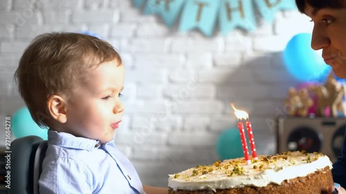 Mother helping her little son blowing out candle on a birthday cake