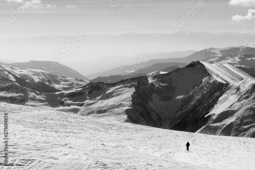 Silhouette of skier on snowy off-piste slope and mountains in haze