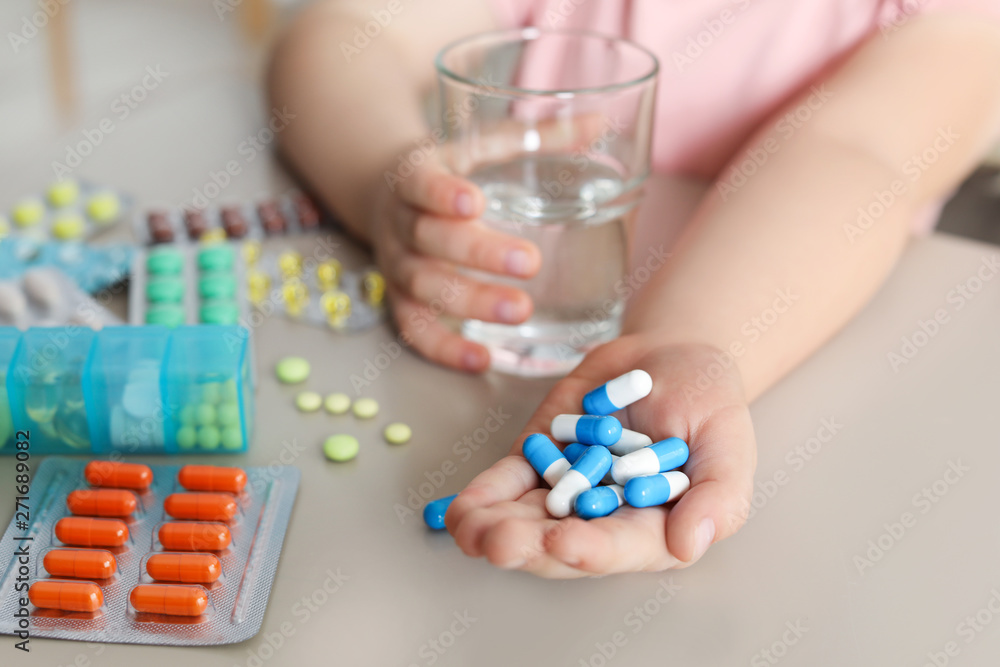 Little child with many different pills and water at table, closeup. Danger of medicament intoxication Little child with many different pills and water at table, closeup. Danger of medicament intoxication