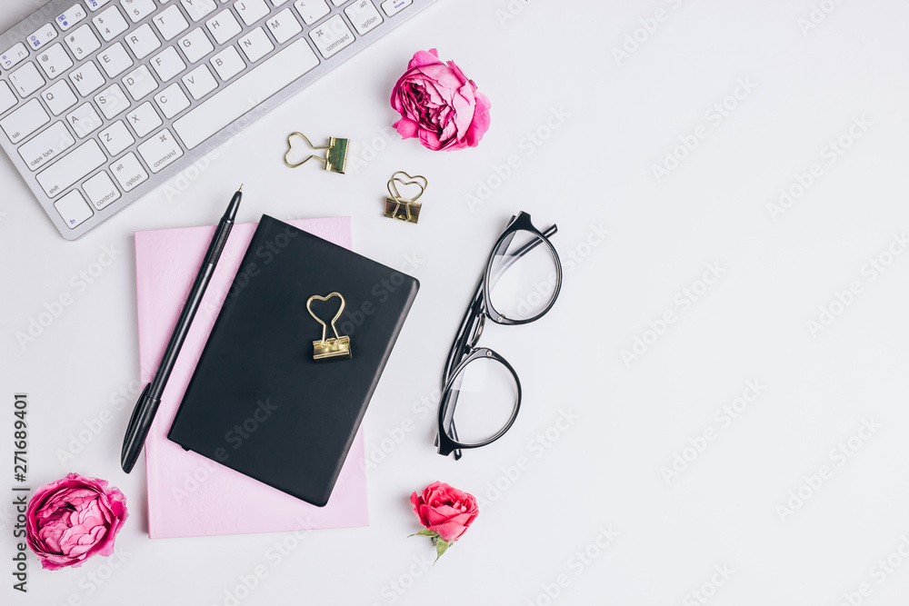 Female work place with computer keyboard, notebook, pen, glasses and flowers