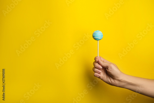 Woman holding bright delicious cake pop on color background, closeup. Space for text