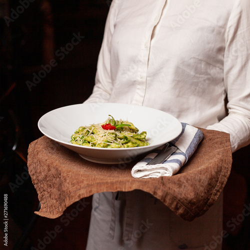 Fototapeta Naklejka Na Ścianę i Meble -  Waiter is holding a tray with bright green pesto pasta
