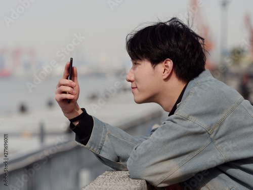 Portrait of a handsome Chinese young man holding his mobile phone, looking for something interesting in internet, mobile phone and the internet take up a lot of teenager's time.