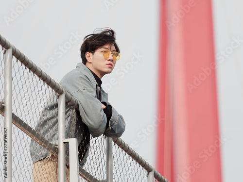 Portrait of a handsome Chinese young man standing on bridge and looking away in wind, has nothing to do just waiting.