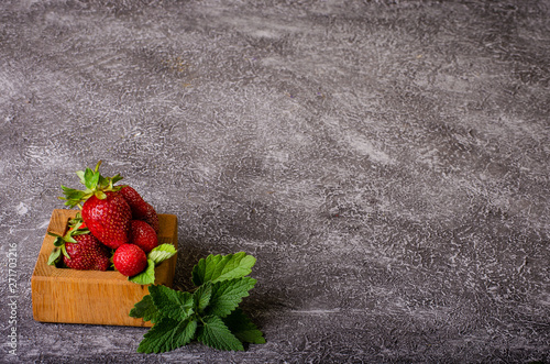 ripe strawberries in a wooden box with peppermint leaves on a dark background advertising space photo