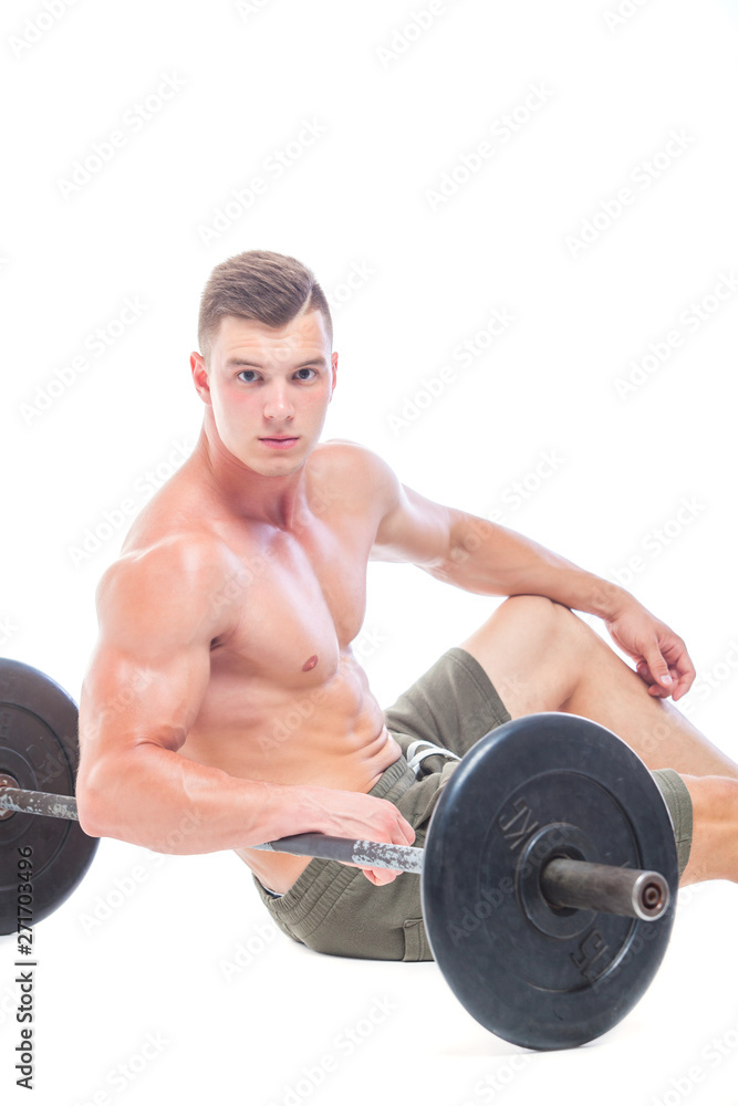 Muscular man working out in studio doing exercises with barbell at biceps, strong male naked torso abs. Isolated on white background. Copy Space. Rest, Sits on the floor at the barbell. Fatigue. Muscular man working out in studio doing exercises with barbell at biceps, strong male naked torso abs. Isolated on white background. Copy Space. Rest, Sits on the floor at the barbell. Fatigue.