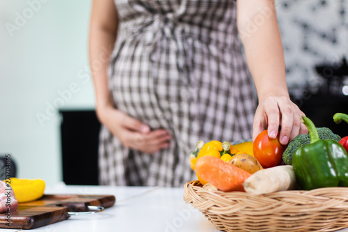 Healthy foods for pregnant women, Young pregnant woman taking fresh tomato from basket.
