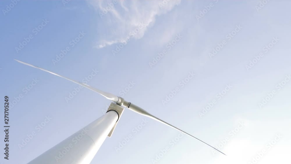 Wind turbine blades rotate against a blue sky with clouds on a sunny day. Energy production with renewable energy. Close up and view from the ground. Wind turbine blades rotate against a blue sky with clouds on a sunny day. Energy production with renewable energy. Close up and view from the ground.