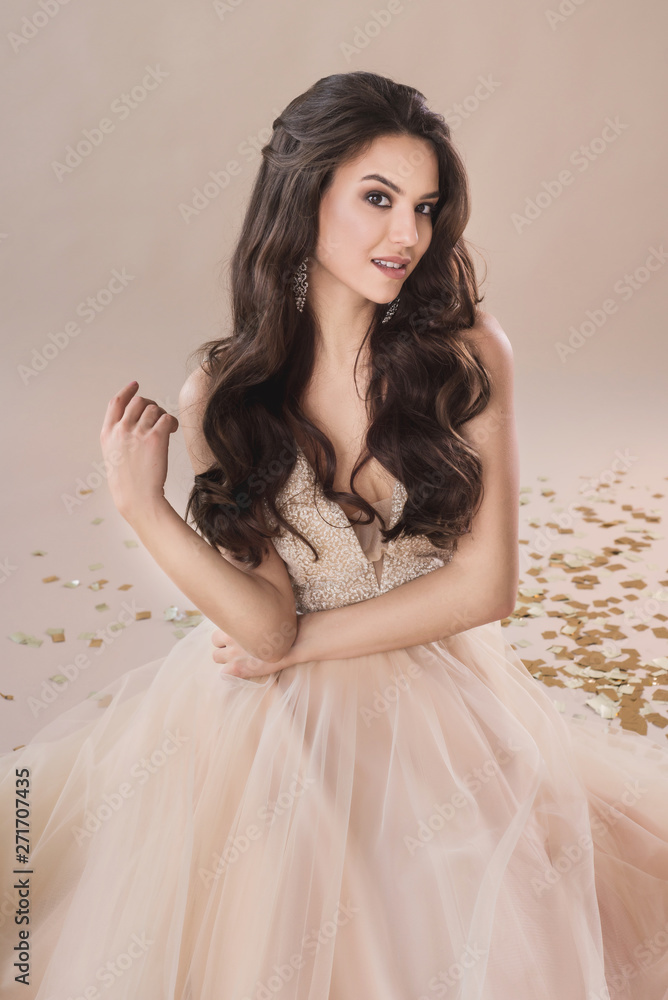 Attractive young brunette woman portrait in evening dress on the beige background Attractive young brunette woman portrait in evening dress on the beige background
