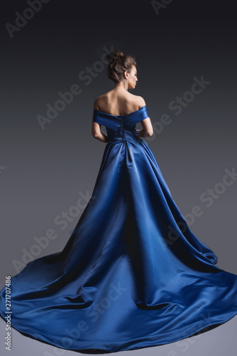 Tablou canvas Beautiful woman in elegant blue dress with plume posing on dark background