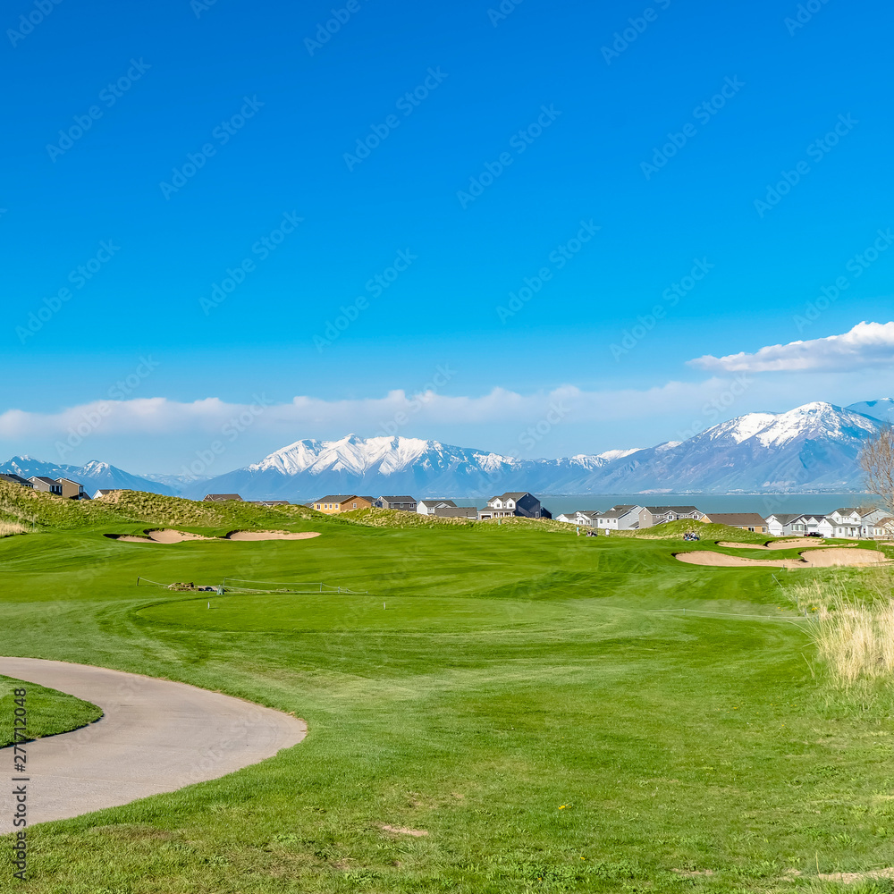 Square Vast grassy field with a curving paved road and houses beyond the slopes
