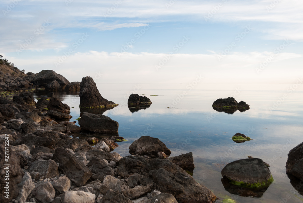 Boulders and rocks in the water. Beautiful seashore with different stones. Blue sky with clouds reflection in water. Nature composition. 