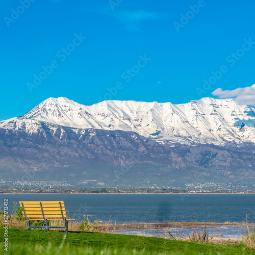 Square Grassy terrain with an empty outdoor bench facing a lake and snowy mountain