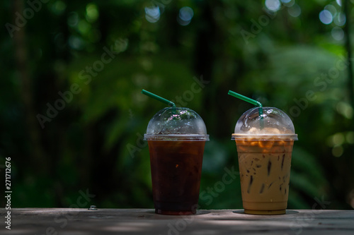 Two  take away plastic cup of iced black coffee americano and iced coffee latte on wood table