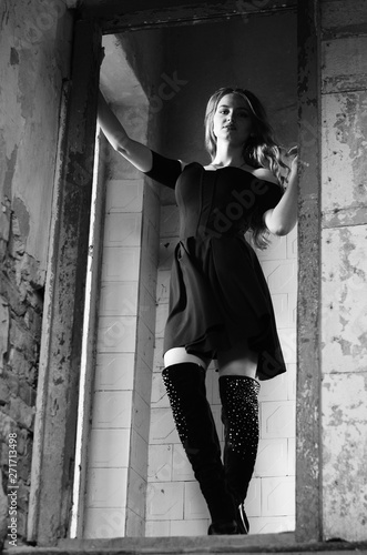 Young beautiful short hair blonde woman in black climbing the stairs, black and white photo. Side view of elegant romantic mysterious lady with movie star look in interior with bricks walls photo