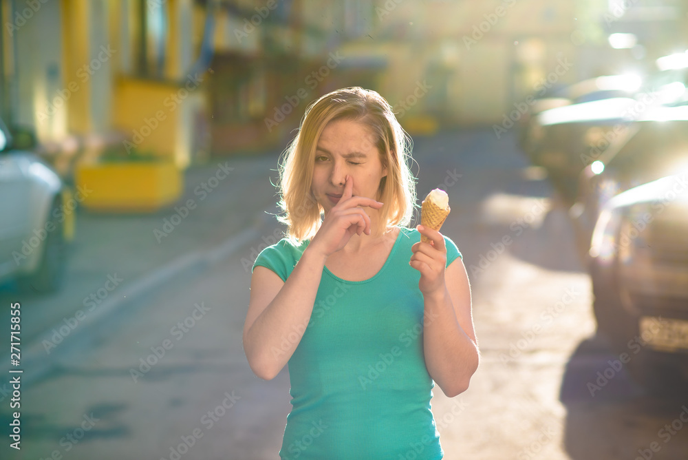 Portrait of a cute girl in a green dress walks in the yard and eats ice cream. A beautiful blonde woman is eating dessert outside on a beautiful summer day. Life is a pleasure vacation
