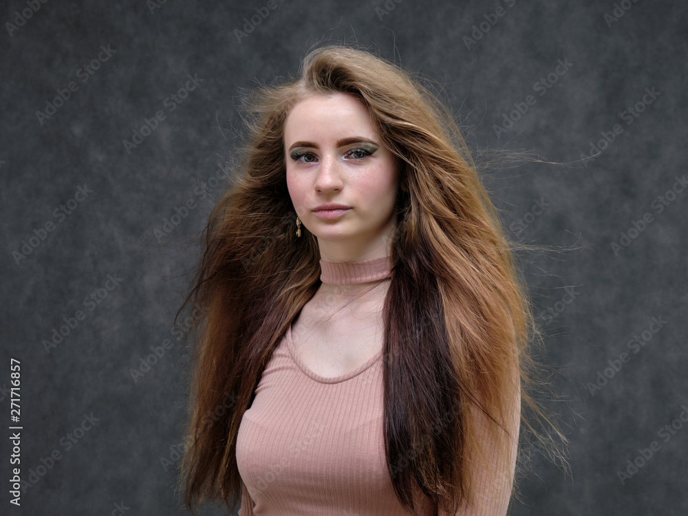 A portrait of a beautiful girl woman on a dark gray background with long beautiful hair in a pink sweater and blue jeans is standing right in front of the camera and smiling. A portrait of a beautiful girl woman on a dark gray background with long beautiful hair in a pink sweater and blue jeans is standing right in front of the camera and smiling.