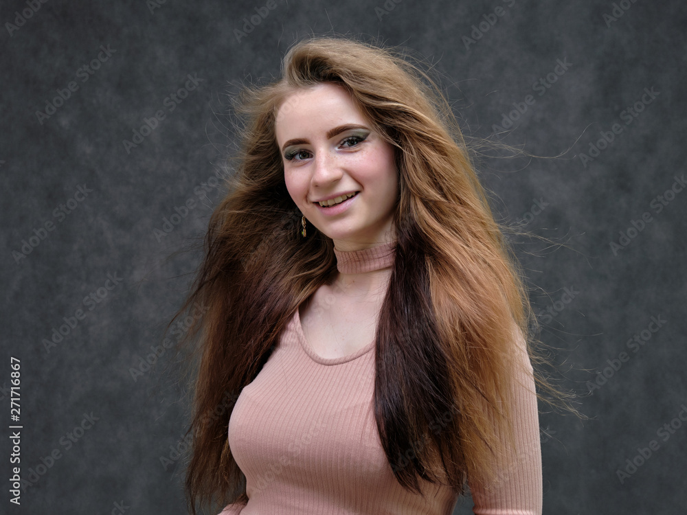A portrait of a beautiful girl woman on a dark gray background with long beautiful hair in a pink sweater and blue jeans is standing right in front of the camera and smiling. A portrait of a beautiful girl woman on a dark gray background with long beautiful hair in a pink sweater and blue jeans is standing right in front of the camera and smiling.