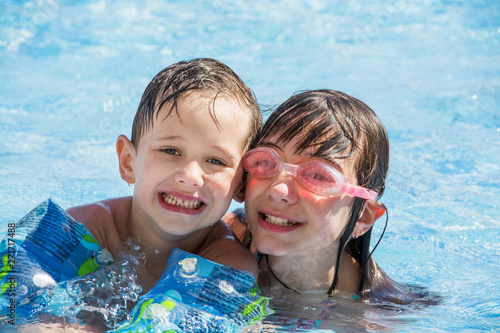 Older sister and younger brother swim in the outdoor children's pool