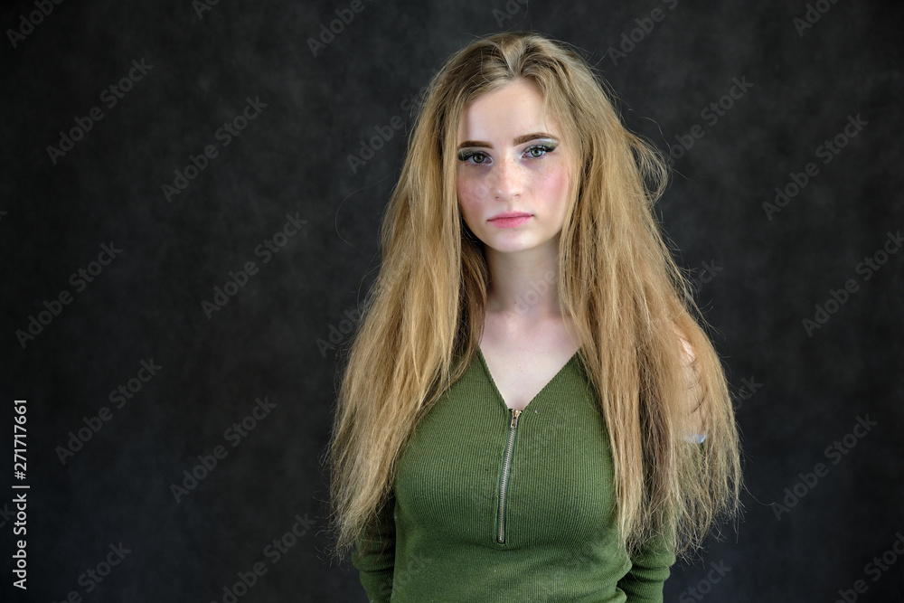 Naklejka premium Photo portrait of a beautiful girl woman on a dark gray background with long flowing beautiful hair in a green dress standing right in front of the camera and smiling.