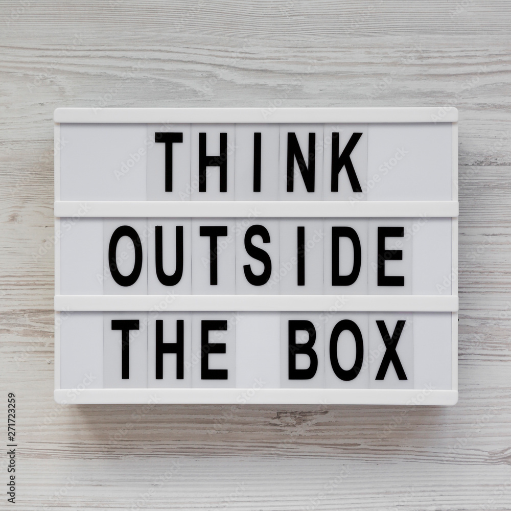 'Think outside the box' words on a modern board on a white wooden background, top view. Flat lay, overhead, from above. Close-up.